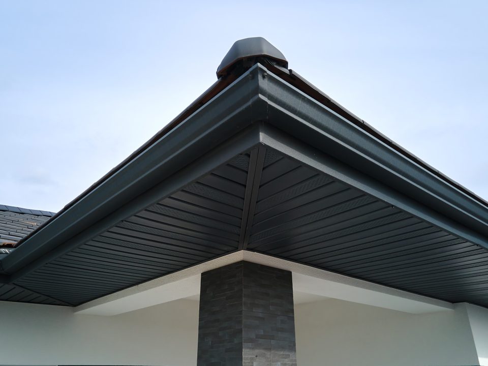 House corner with brown metal planks siding and roof with steel gutter rain system